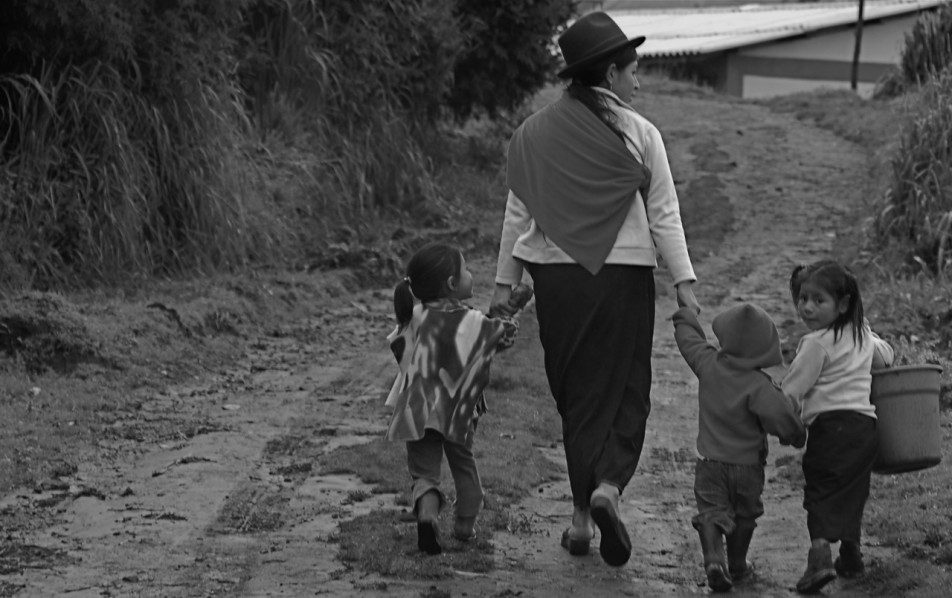 Una madre cammina lungo una strada di campagna con tre bambini, mano nella mano